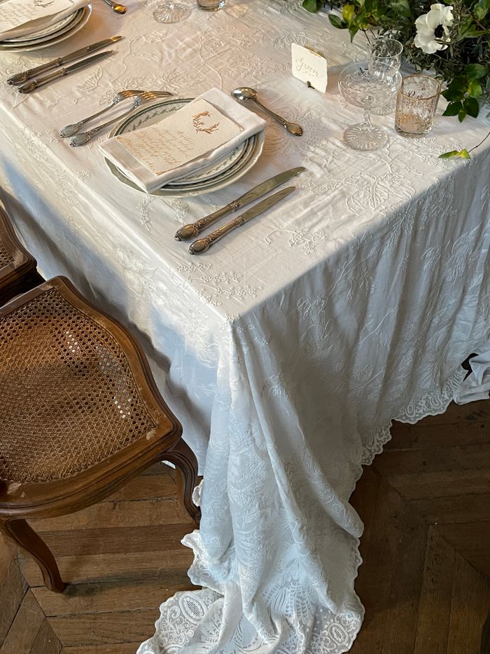 Elegant close-up of a wedding reception table setting with ornate tablecloth and vintage cutlery.